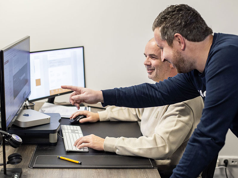 Michel en Ron aan het werk op de computer van Ron. Michel wijst naar het scherm